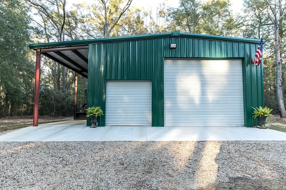 A finished green metal garage with a lean to on the side.